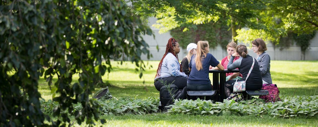 students sit in a circle in grass at Grand Valley